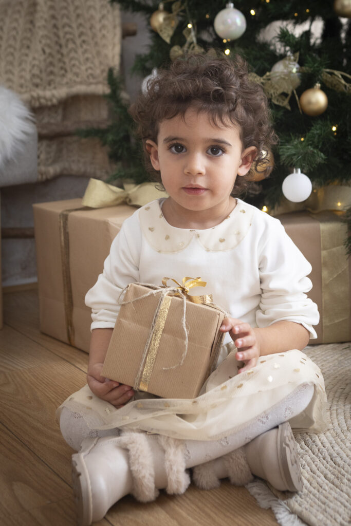 bimba con regalo abito bianco davanti all'albero di natale (1 di 1)